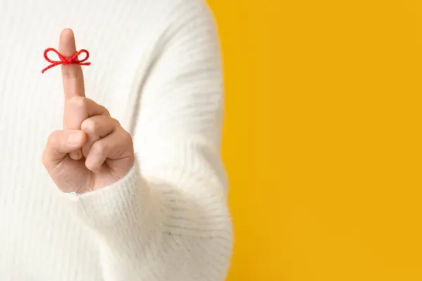 Woman with red bow on index finger against yellow background. Reminder concept