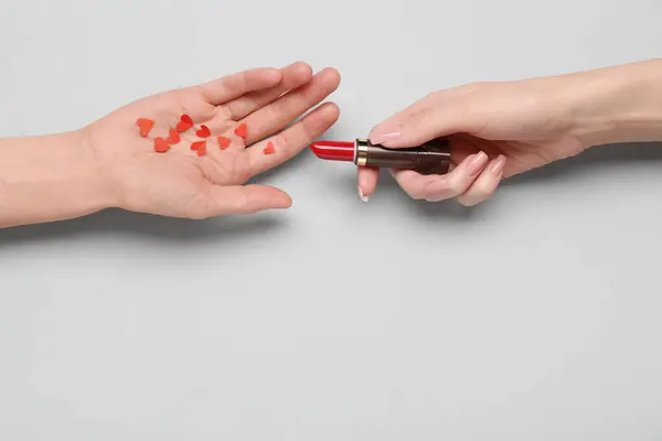 Female hands with red lipstick and paper hearts on grey background