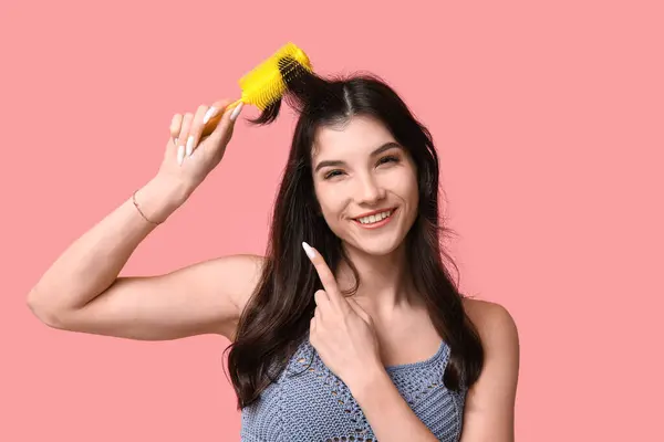 ピンクの背景に黄色い髪のブラシを指している美しい若い女性 — ストック写真