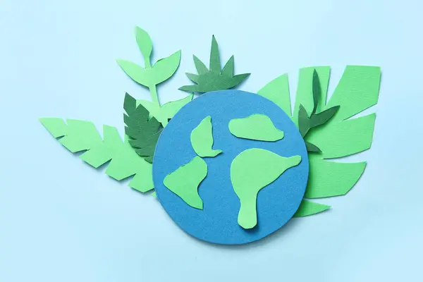 Paper planet Earth with green leaves on blue background. Earth day celebration.
