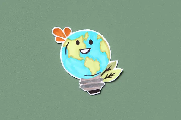 Paper smiling planet Earth in shape of bulb on green background. Earth Day celebration.