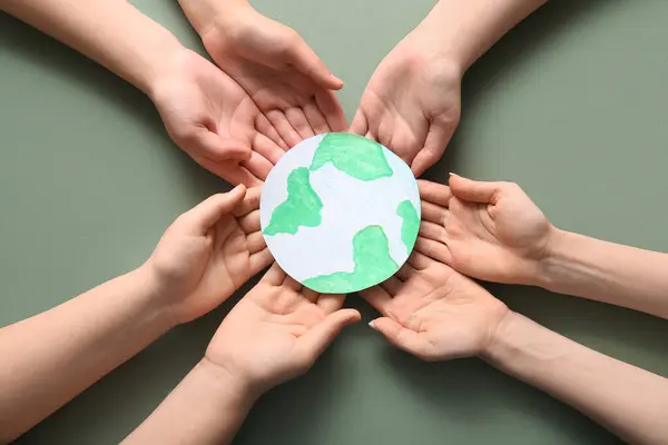 Hands holding paper planet Earth on green background. Earth Day celebration.