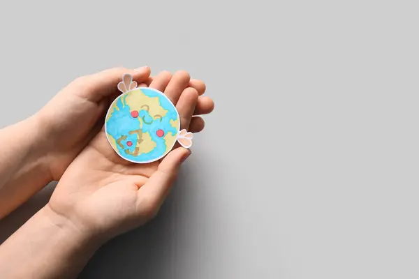 Female hands holding paper planet Earth on white background. Earth Day celebration.