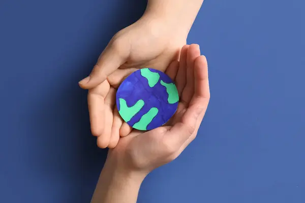 Female hands holding paper planet Earth on blue background. Earth Day celebration.