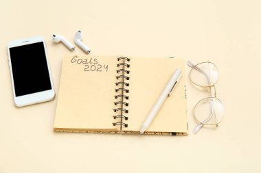 Listesi boş bir defter, bej arka planda cep telefonu ve gözlük. Yeni yıl hedefleri