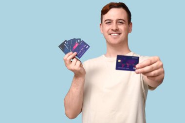 Mavi arka planda kredi kartı olan genç bir adam.