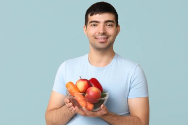 Mavi arka planda A vitamini bakımından zengin bir yiyecek kasesi olan genç adam.