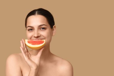 Bej arka planda taze greyfurt olan güzel genç bir kadın.