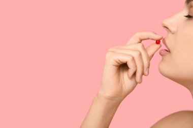 Güzel genç bayan pembe arka planda A vitamini kapsülü alıyor, yakın plan.