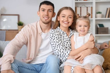 Mutlu ebeveynler ve küçük kızları evde kanepede kucaklaşıyorlar.