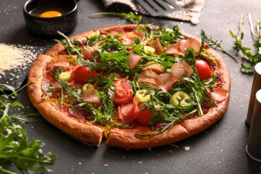 Domatesli lezzetli pizza ve siyah arka planda roka.