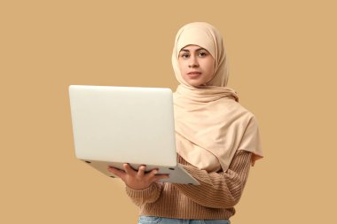 Bej arka planda modern dizüstü bilgisayarı olan Müslüman bir Afro-Amerikalı kadın.