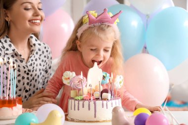 Annesiyle taç giymiş şirin küçük bir kız ve evde doğum gününü kutlayan bir pasta.