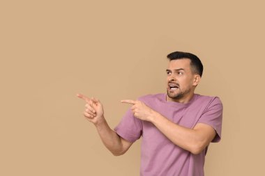 Yakışıklı, utangaç genç bir adam kahverengi arka planda bir şeye işaret ediyor.