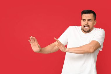 Kırmızı arka plandaki yakışıklı, utangaç genç adam.