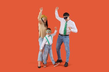 Kostümlü mutlu aile ve turuncu arka planda dans eden karnaval maskeleri.