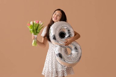 Gümüş renkli hava balonu olan güzel bir Asyalı kadın figür 8 ve kahverengi arka planda bir buket güzel lale. Uluslararası Kadınlar Günü