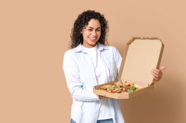 Beautiful young happy African-American woman with delicious pizza on beige background
