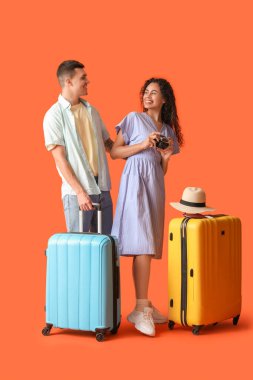 Çantalı ve turuncu arka planda fotoğraf makinesi olan iki turist.