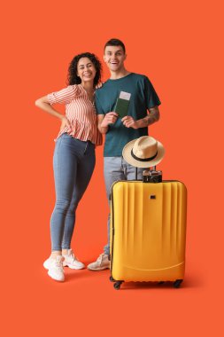 Turuncu arka planda bavulu ve pasaportu olan iki turist.