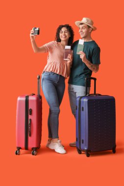 Çantalı ve pasaportlu turistler turuncu arka planda selfie çekiyorlar.