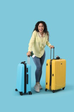 Mavi arka planda bavulları ve pasaportu olan genç bir Afro-Amerikalı bayan turist.