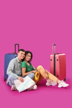 Pembe arka planda oturan bavullu ve haritalı iki turist.