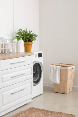 Çamaşır makinesi ve çamaşır sepetiyle aydınlatma odasının içinde.