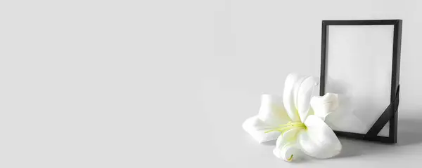 Blank funeral frame and lily flower on light background with space for text