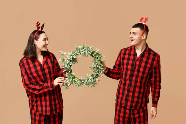 Mutlu Genç Çift Noel Pijamalarıyla Bej Arkaplanlı Çelenkleriyle — Stok fotoğraf