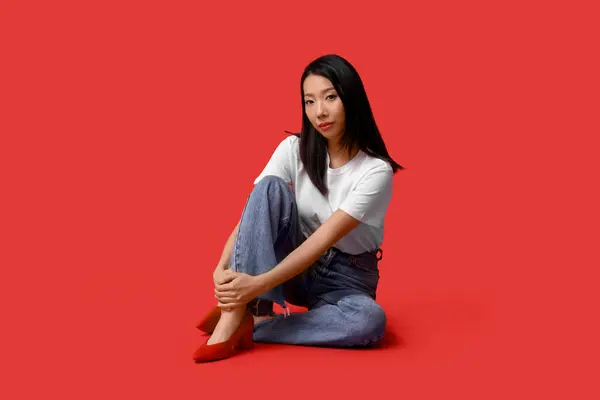 Belle Jeune Femme Asiatique Jean Élégant Assis Sur Fond Rouge — Photo