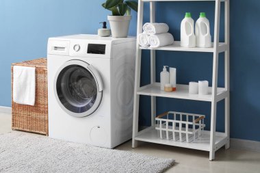 Çamaşır sepeti, çamaşır makinesi ve raf ünitesi olan odanın içi.