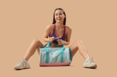 Bej arka planda oturan çantalı genç bir bayan.