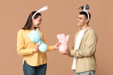 Paskalya tavşanı kulaklı mutlu genç çift ve bej arka planda hediyeler