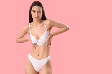 Pembe arka planda beyaz iç çamaşırlı zayıf genç bir kadın.