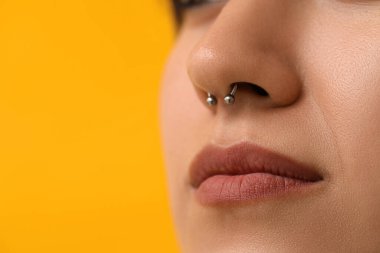 Sarı arka planda burun piercingli şık genç kadın, yakın plan.