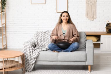 Evdeki kanepede sopayla glukofon çalan mutlu olgun bir kadın.