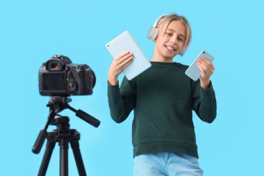 Mavi arka planda video kayıt cihazlarıyla kulaklık takan genç blogcu