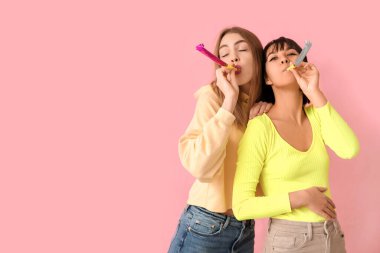 Pembe arka planda parti düdüğü çalan güzel genç kadınlar. 1 Nisan şakası