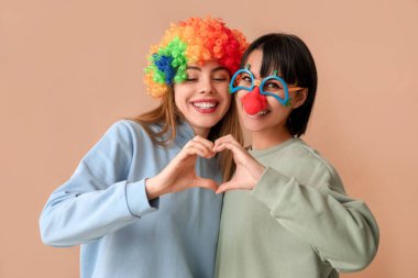 Kahverengi arka planda kalp hareketi gösteren komik palyaço kılığına girmiş güzel genç kadınlar. 1 Nisan şakası