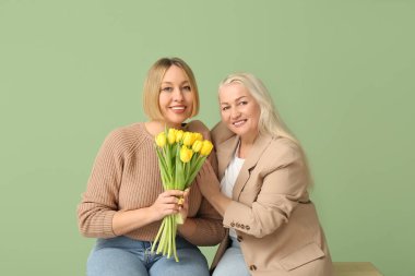 Annesiyle yetişkin bir kadın ve bir buket lale yeşil arka planda bankta oturuyor. Uluslararası Kadınlar Günü kutlamaları