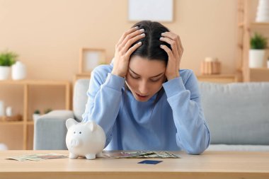 Evde domuz kumbarası, kredi kartları ve parası olan stresli genç bir kadın.
