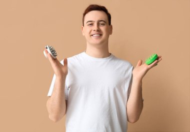 Kahverengi arka planda saç derisi masaj aletleri olan genç bir adam.