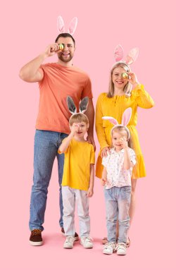 Pembe arka planda Paskalya yumurtaları olan tavşan kulaklı mutlu bir aile.