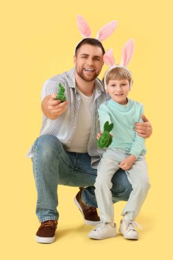 Mutlu baba ve küçük oğlu tavşan kulaklı, sarı arka planda Paskalya tavşanları