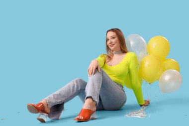 Mavi arka planda oturan balonlu genç bir kadın.