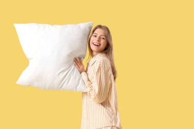 Sarı arka planda yastıklı pijamalı genç bir kadın.