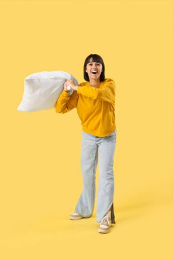 Sarı arka plana yastık atan genç bir kadın.