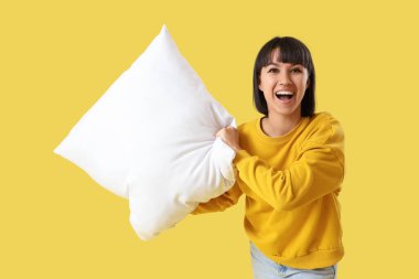 Sarı arka plana yastık atan genç bir kadın.