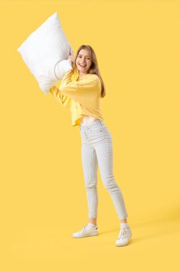 Sarı arka plana yastık atan genç bir kadın.